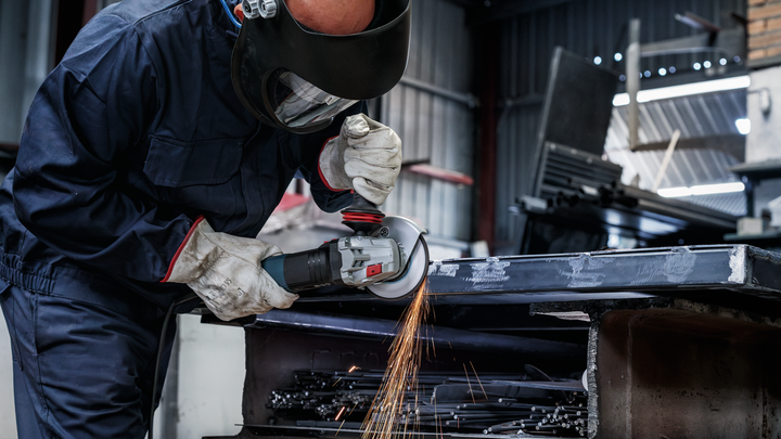 Eine Person mit Sicherheitsausrüstung schleift einen Metallstrahl und erzeugt dabei Funken.