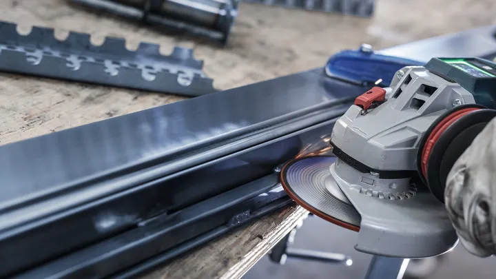 Eine Person mit Schutzausrüstung schleift einen Metallträger mit einem Winkelschleifer.