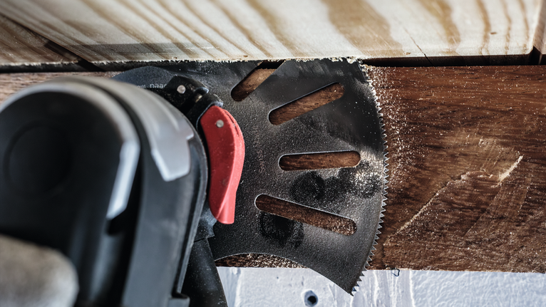 Oszillierendes Multifunktionswerkzeug schneidet durch Holz in der Nähe eines Bretts.
