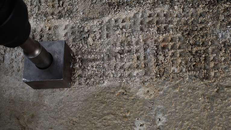 Metallwerkzeug zum Eindrücken quadratischer Vertiefungen in raue Betonoberflächen.