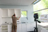 Eine Person richtet einen Küchenschrank mithilfe eines Lasernivelliergeräts auf einem Stativ aus.