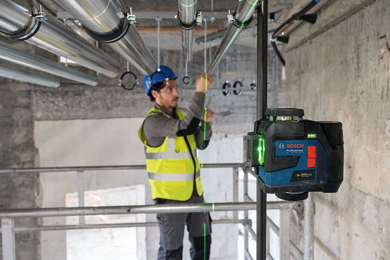 Eine Person mit Sicherheitsausrüstung richtet Rohre mit einem Lasernivelliergerät aus.