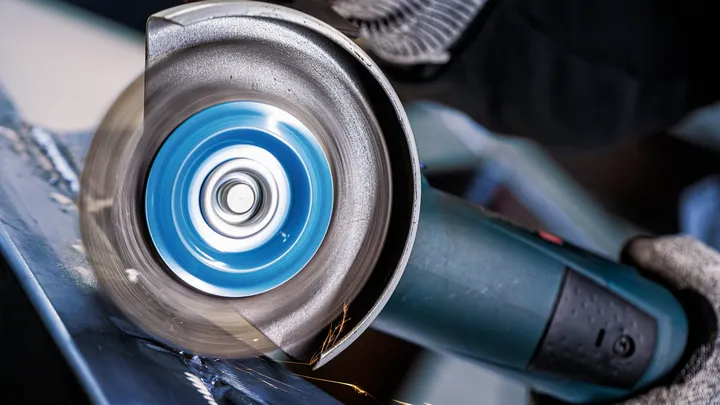 Eine Person mit Sicherheitsausrüstung verwendet einen Winkelschleifer zum Schneiden von Metall.