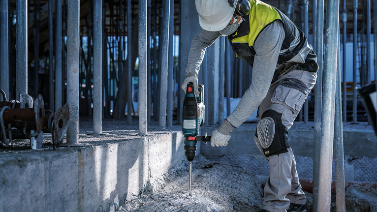 Eine Person mit Sicherheitsausrüstung bohrt auf einer Baustelle in Beton.
