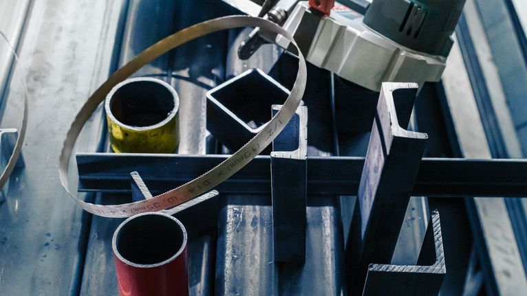 Bandsäge über verschiedenen Metallrohren und -stangen auf einer Werkbank.
