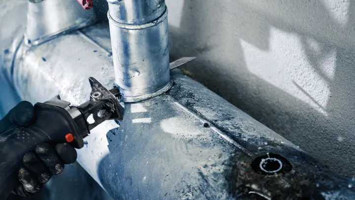 Eine Person mit Sicherheitsausrüstung schneidet mit einem Elektrowerkzeug ein Metallrohr.