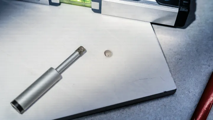 Diamantbohrer und Wasserwaage auf einer weißen Fliese mit einem frisch gebohrten Loch.