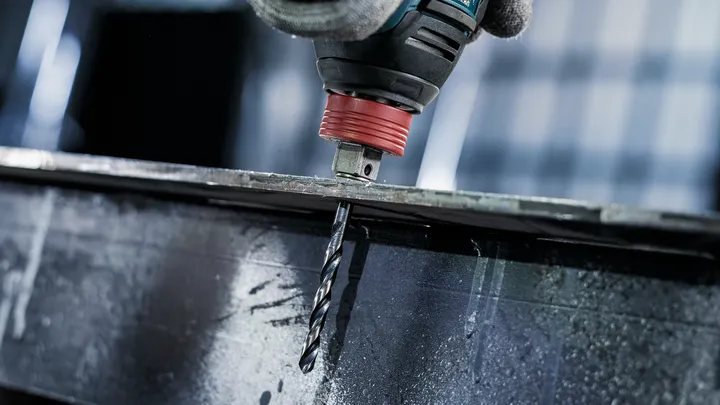 Person mit Sicherheitsausrüstung bohrt durch einen Metallträger.