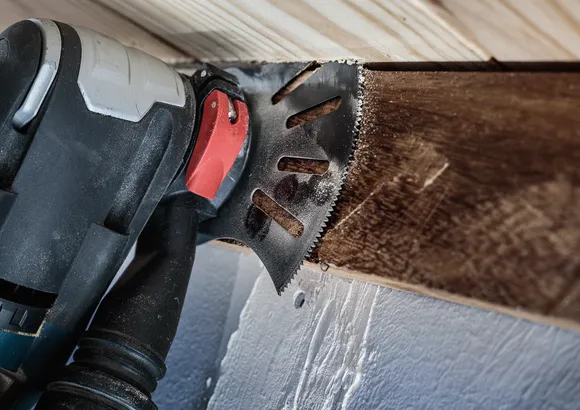 Oszillierendes Elektrowerkzeug schneidet in einem engen Raum durch einen Holzbalken.