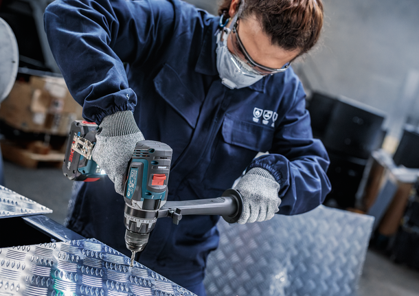 Person mit Schutzausrüstung bohrt in eine Metallplatte.