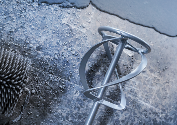 Farbmischerpaddel ruht auf einer strukturierten Oberfläche mit nassem Beton.