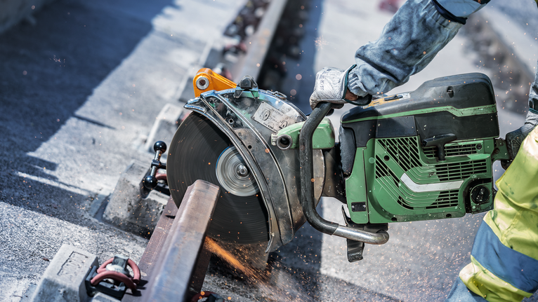 Eine Person mit Sicherheitsausrüstung schneidet mit einer Motorsäge eine Metallschiene durch.