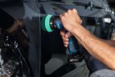 Eine Person poliert eine schwarze Autotür mit einer Akku-Poliermaschine.