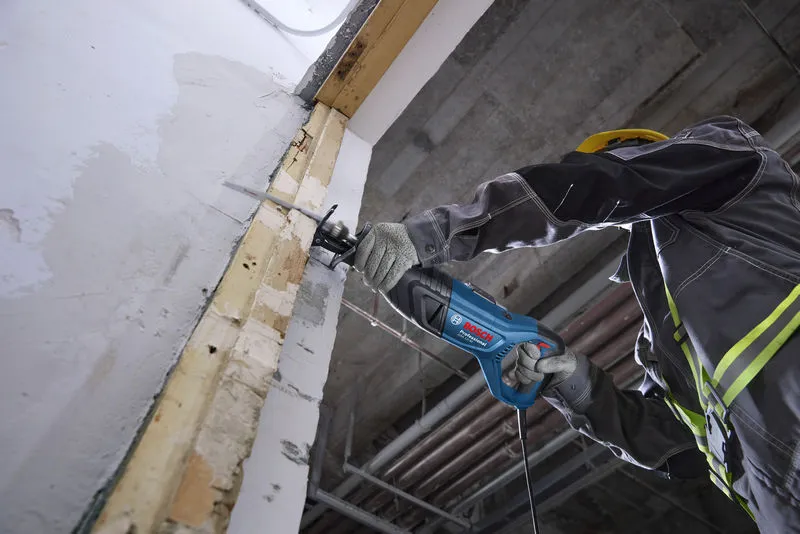 Eine Person mit Sicherheitsausrüstung schneidet mit einer Säbelsäge in eine Wand.