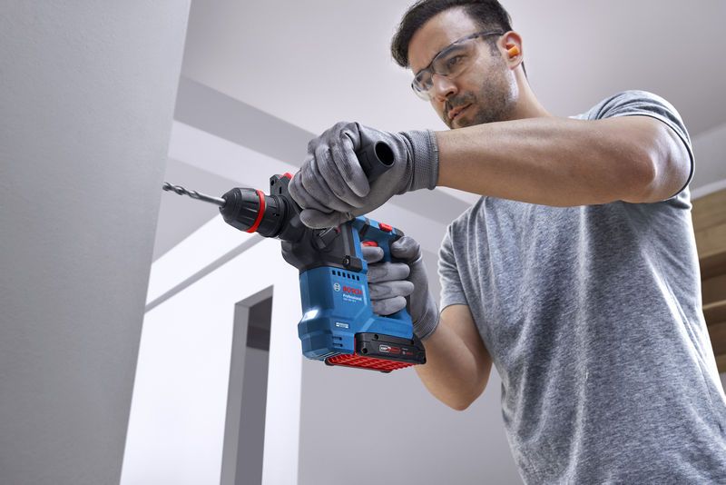 Eine Person mit Schutzausrüstung bohrt mit einem Akku-Bohrhammer in eine Betonwand.