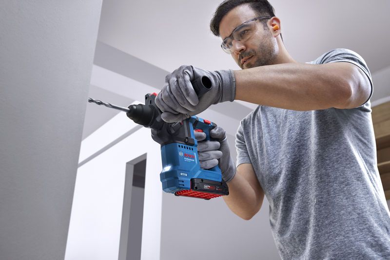 Person mit Schutzausrüstung bohrt mit Bohrhammer in eine Wand.