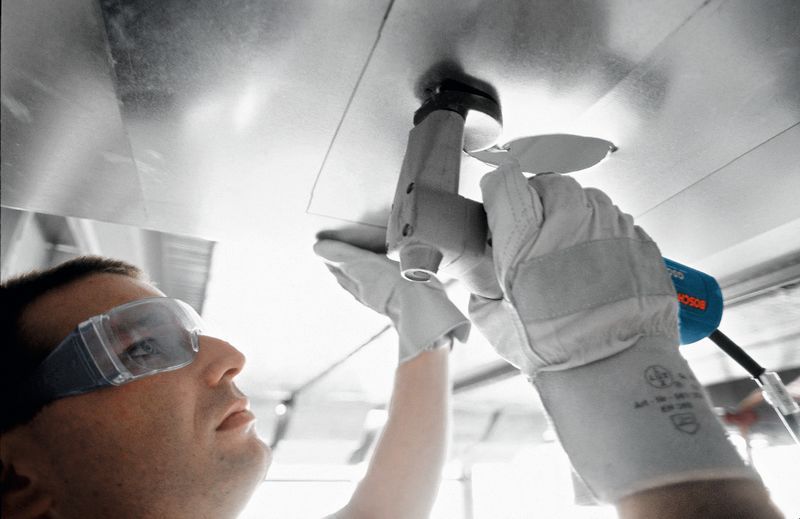 Eine Person mit Sicherheitsausrüstung schneidet mit einer Schere ein Metallblech.