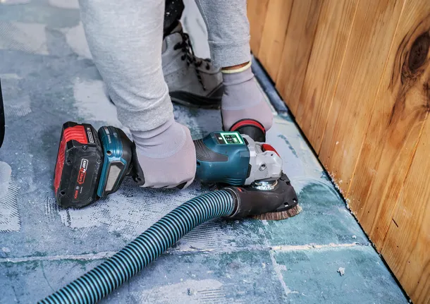 Eine Person mit Sicherheitsausrüstung schleift einen Betonboden in der Nähe einer Holzwand.