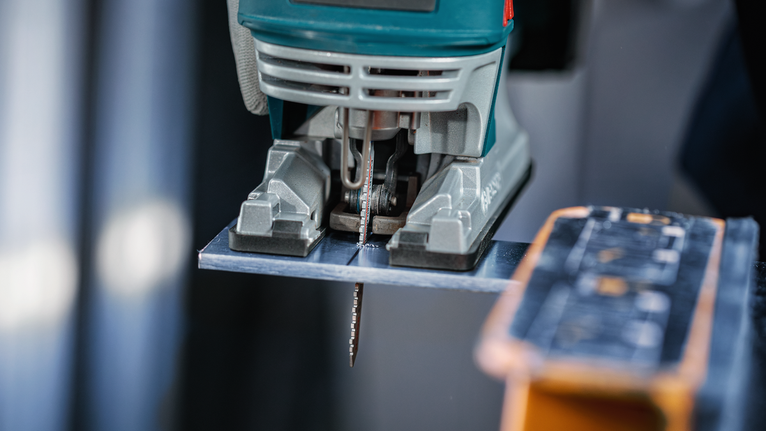 Stichsäge schneidet ein Metallblech auf einer Werkbank.