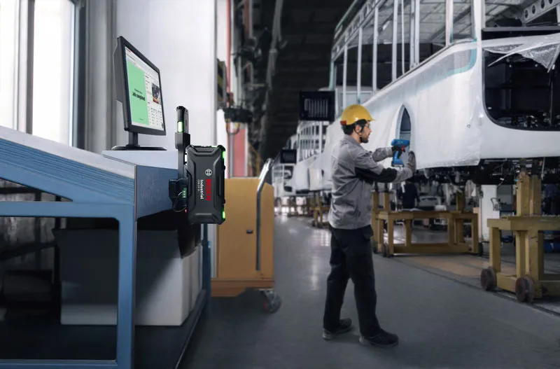 Eine Person, die Schutzausrüstung trägt, montiert in einer Fabrik mit einem Elektrowerkzeug einen Fahrzeugrahmen.