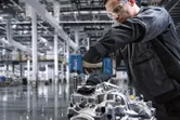 Eine Person mit Schutzausrüstung bearbeitet mit einer Akku-Bohrmaschine ein Motorteil.
