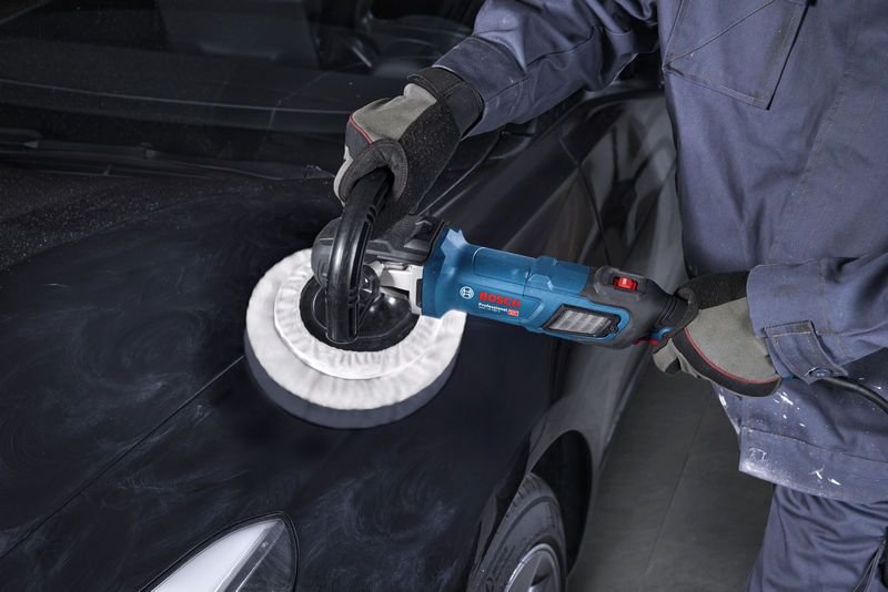 Eine Person mit Sicherheitsausrüstung verwendet eine Poliermaschine auf einer schwarzen Motorhaube.