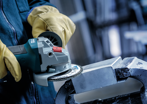 Eine Person mit Schutzausrüstung schleift einen Metallblock mit einem Winkelschleifer.