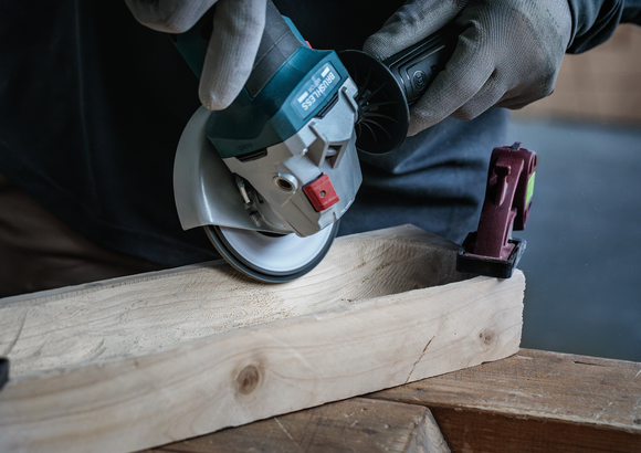 Eine Person mit Sicherheitsausrüstung verwendet ein Elektrowerkzeug, um ein Stück Holz zu schneiden.