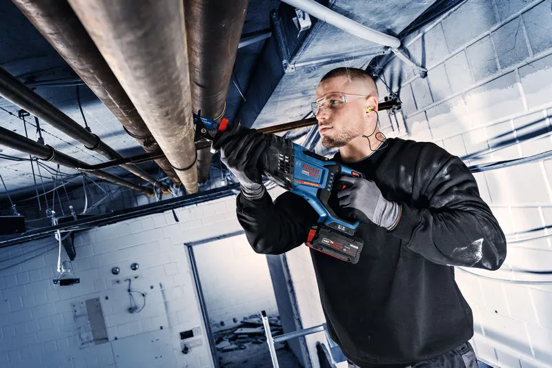 Eine Person mit Sicherheitsausrüstung verwendet eine kabellose Säbelsäge, um Metallrohre zu schneiden.