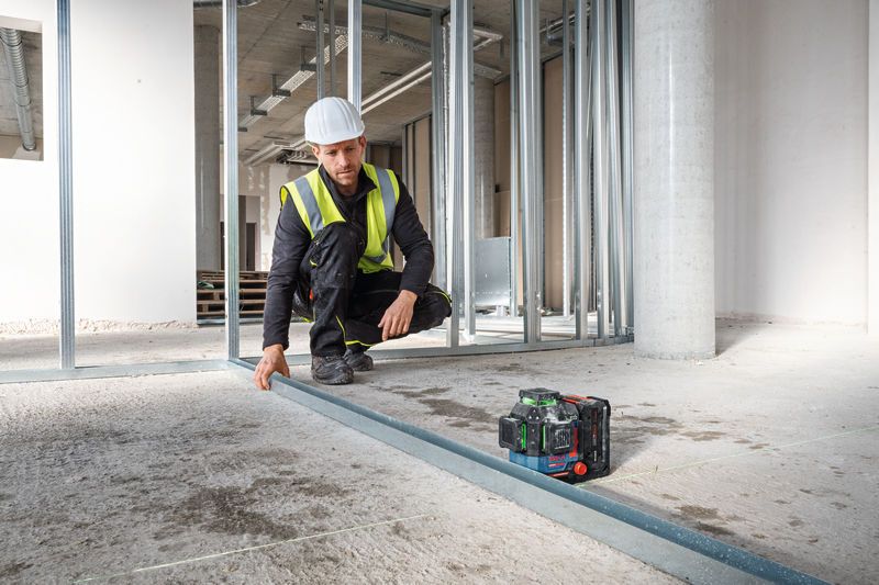 Eine Person mit Sicherheitsausrüstung richtet eine Metallschiene mit einem Lasernivelliergerät aus.