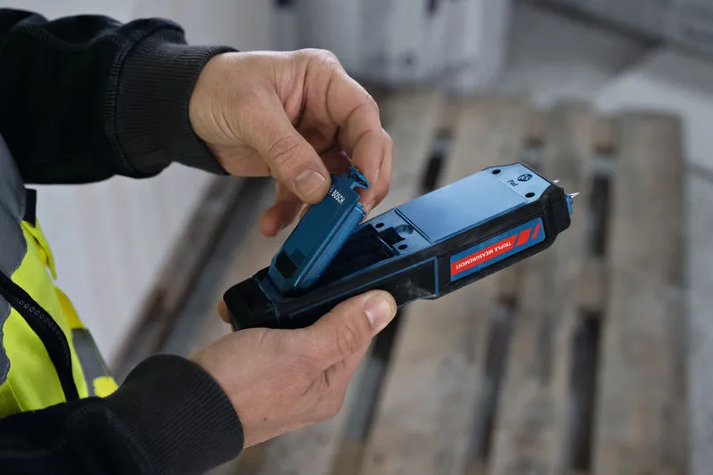 Eine Person mit Schutzausrüstung legt eine Batterie in ein Materialfeuchtemessgerät ein.