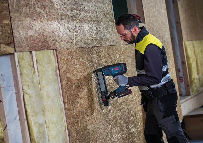 Eine Person, die Schutzausrüstung trägt, befestigt mit einem Akku-Tacker Paneele an einer Wand.