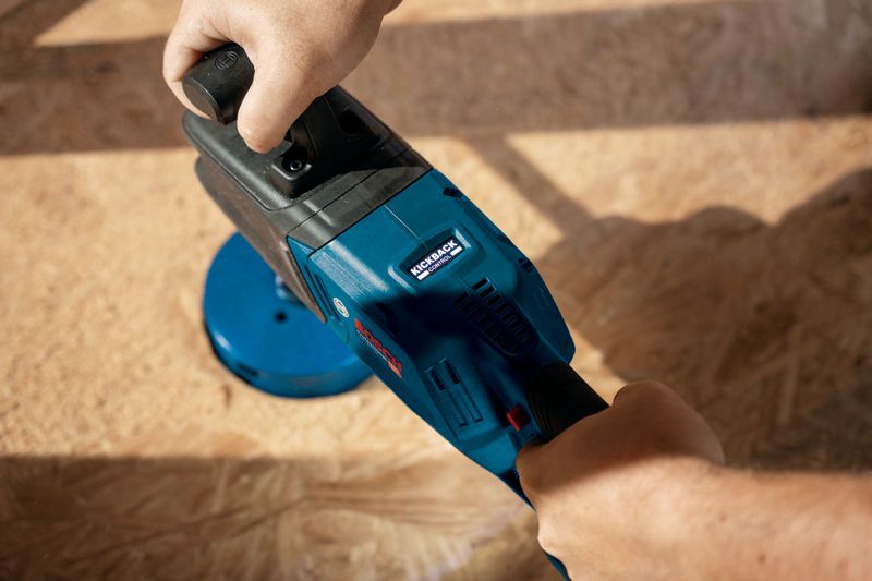 Eine Person bedient eine blaue Akku-Winkelbohrmaschine auf einer Holzoberfläche.