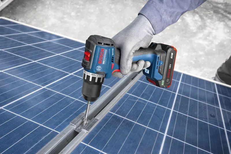 Eine Person, die Schutzausrüstung trägt, benutzt einen Akkuschrauber an einem Solarpanelrahmen.