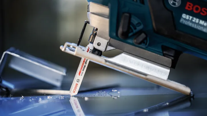 Eine Stichsäge schneidet durch eine Glasscheibe, in deren Nähe verstreute Glassplitter liegen.