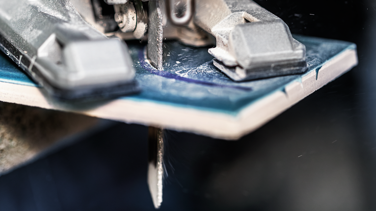 Stichsägeblatt schneidet durch eine blaue Keramikfliese.