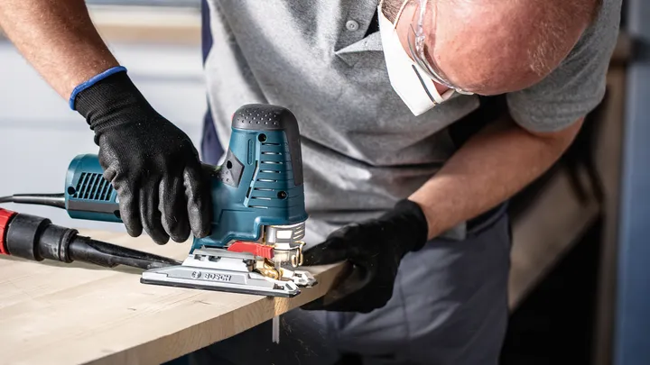 Eine Person mit Sicherheitsausrüstung schneidet Holz mit einer elektrischen Stichsäge.