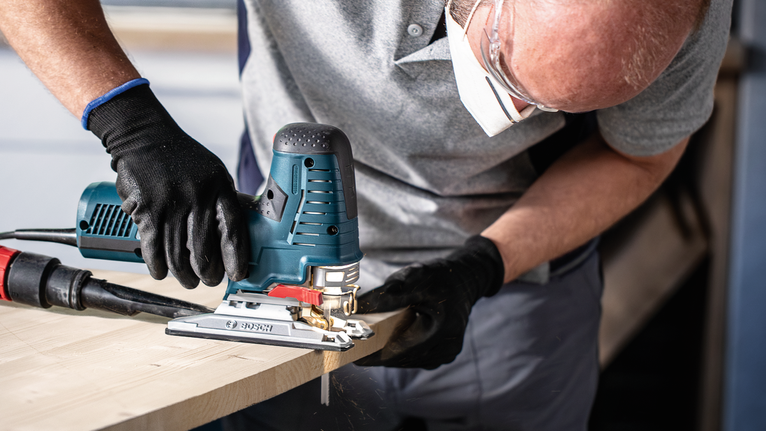 Eine Person mit Sicherheitsausrüstung schneidet Holz mit einer elektrischen Stichsäge.