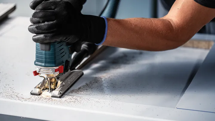 Person mit Sicherheitsausrüstung schneidet Holz mit einer Stichsäge.