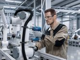 Ein Arbeiter in Schutzausrüstung bedient einen Akkuschrauber an einem Industrieroboterarm.