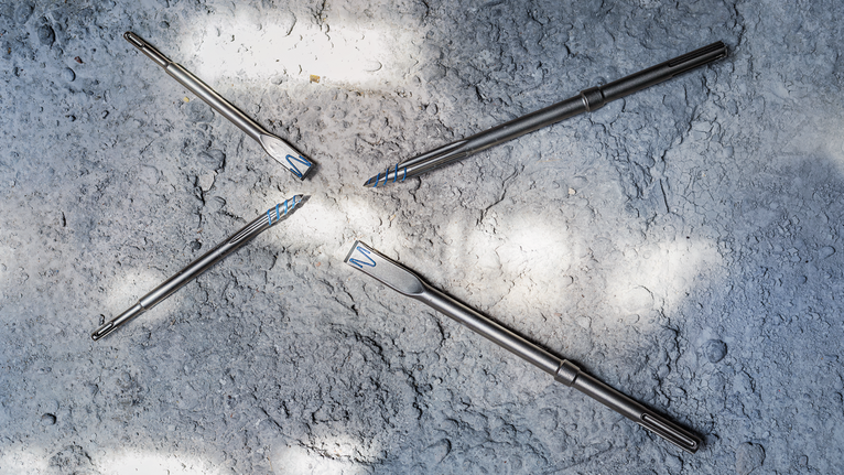 Auf einer rauen Betonoberfläche sind vier Metallbohrer angeordnet.