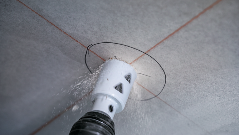 Mit einer Lochsäge wird eine kreisrunde Öffnung in eine Deckenplatte gebohrt.