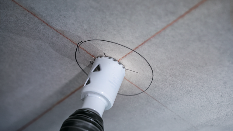 Mit einer Lochsäge wird eine kreisrunde Öffnung in eine Deckenplatte gebohrt.