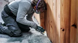 Eine Person in Schutzausrüstung schleift Beton in der Nähe einer Holzwand.