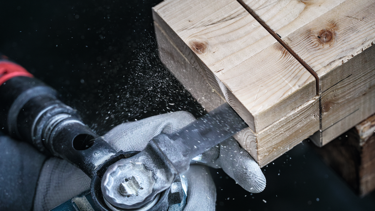Eine Person, die Schutzausrüstung trägt, schneidet einen Holzbalken mit einer Kreissäge.