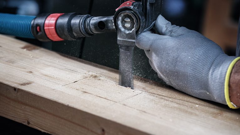 Eine Person, die Schutzausrüstung trägt, schneidet ein Holzbrett mit einer Säbelsäge.