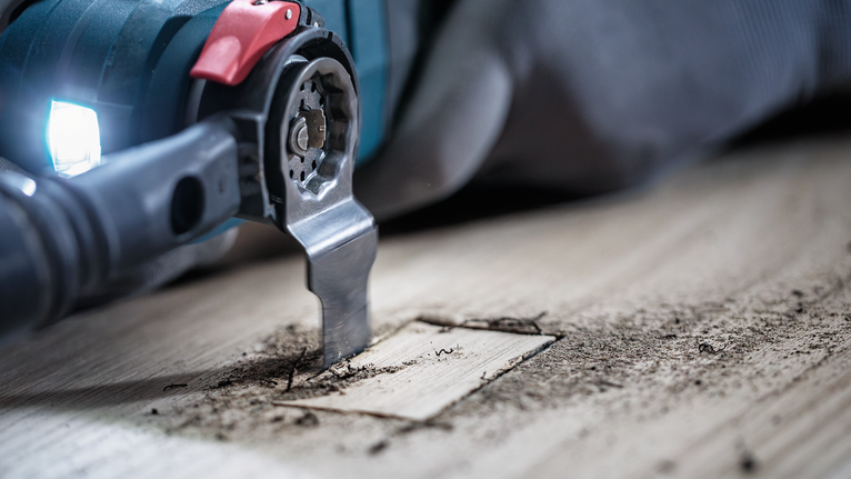 Eine Person, die Schutzausrüstung trägt, schneidet mit einem Multifunktionswerkzeug ein präzises Quadrat in Holz.