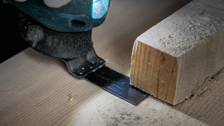 Oszillierendes Sägeblatt schneidet ein Holzbrett in Nahaufnahme aus der Werkstatt.