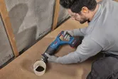Eine Person, die Schutzausrüstung trägt, benutzt eine akkubetriebene Säbelsäge, um ein PVC-Rohr zu durchtrennen.