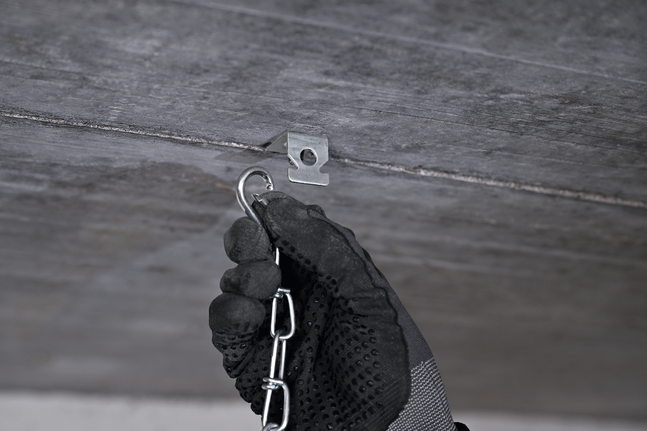 Eine Person, die Schutzausrüstung trägt, hängt eine Kette an einen metallenen Deckenhaken.